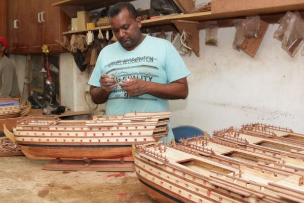 A craftsman working on the rigging of a ship model in a Mauritian workshop.